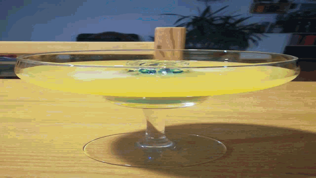 a glass with a yellow liquid in it is on a wooden table