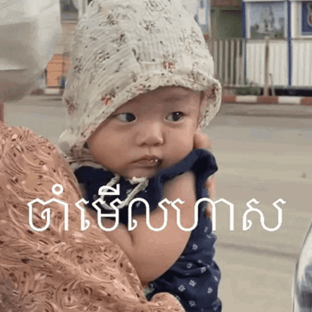 a baby wearing a hat is being held in a woman 's arms and the baby is looking at the camera