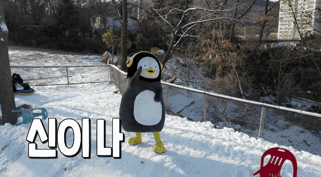 a stuffed penguin is standing in the snow with a red chair in front of it