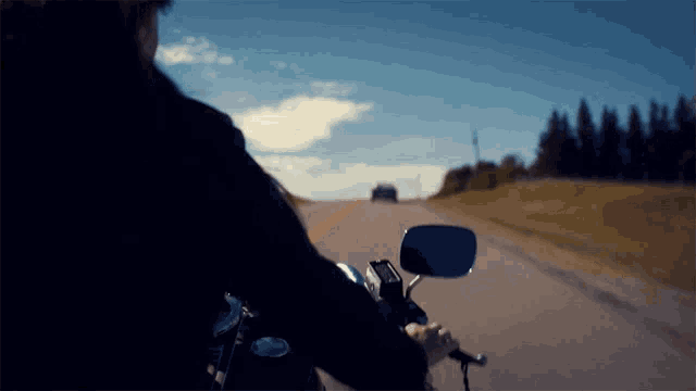 a person riding a motorcycle down a road with a car behind them