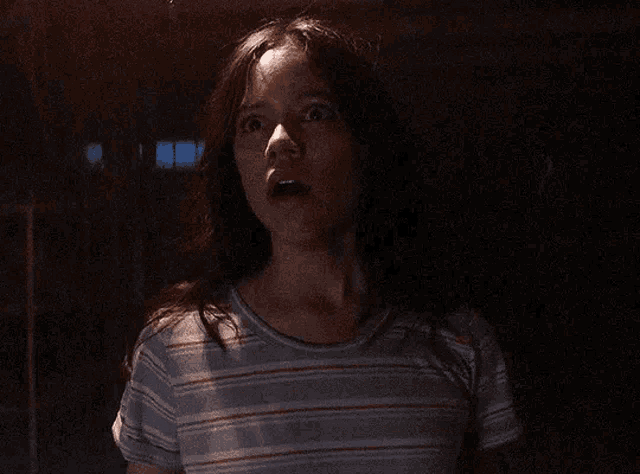 a woman in a striped shirt is standing in the dark with her mouth open .