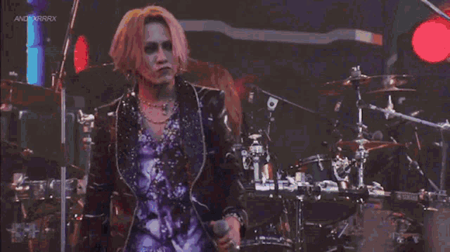 a man is standing on a stage in front of a drum set and a microphone .