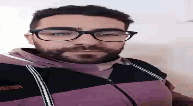 a man with glasses and a beard is wearing a purple jacket .
