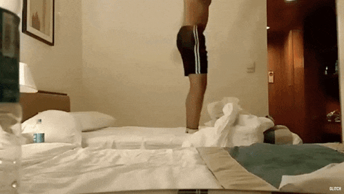 a man without a shirt is jumping on a bed in a hotel room ..