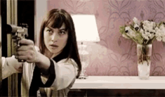 a woman is pointing a gun in a room with flowers in a vase