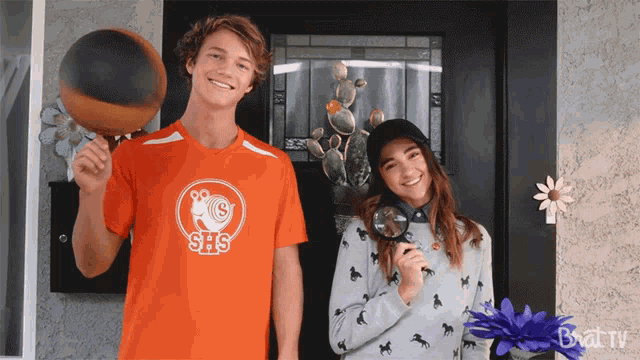 a boy wearing an orange shirt that says shs holds a basketball and a girl holds a magnifying glass