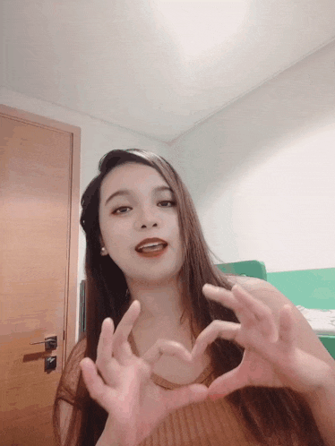 a woman making a heart with her hands in front of a door