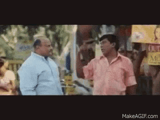 a man in a pink shirt is talking to another man in a blue shirt on a street .