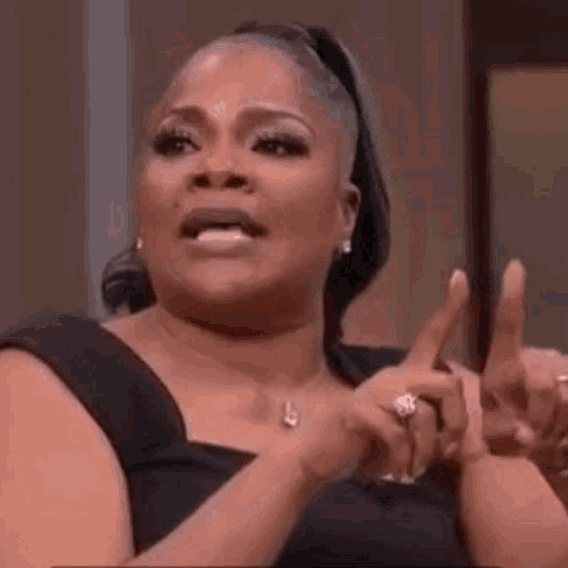a woman in a black dress is making a funny face while holding her hands up .