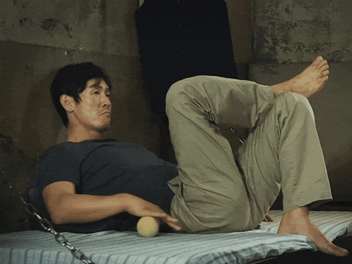 a man is laying on a bed with his legs crossed and a ball in his hand