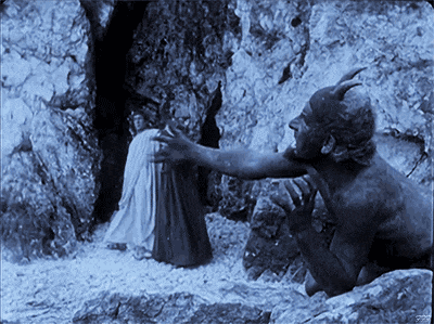 a man with horns is reaching out to a woman