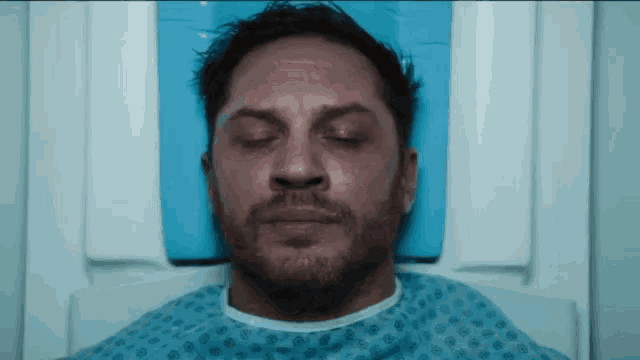 a man is laying in a hospital bed with his eyes closed and a beard .