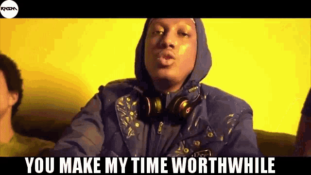 a man wearing headphones and a hooded jacket is sitting on a couch .