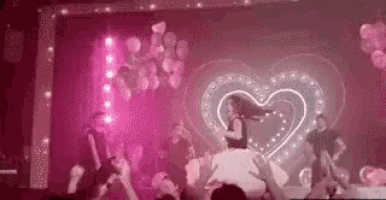 a woman is singing into a microphone on a stage with a heart in the background .
