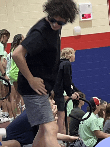 a boy wearing sunglasses stands in front of a digital clock that says 10:37 on it