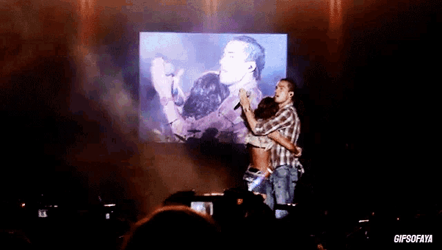 a man is hugging a woman on a stage in front of a screen that says gifsofaya