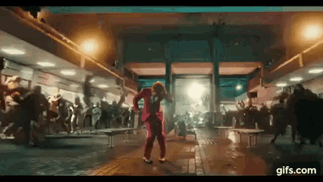 a man in a red suit is dancing in front of a crowd of people in a building .