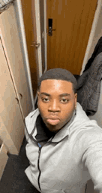 a man is taking a selfie in a hallway while wearing a grey jacket .