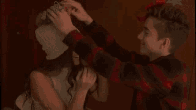a boy and a girl are sitting next to each other and the boy is putting a bow on the girl 's hat .