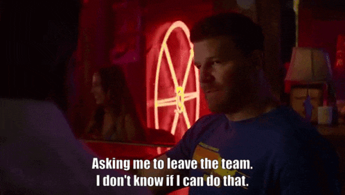 a man is sitting in front of a neon sign that says " asking me to leave the team "