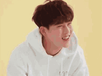 a young man in a white hoodie is smiling and laughing .