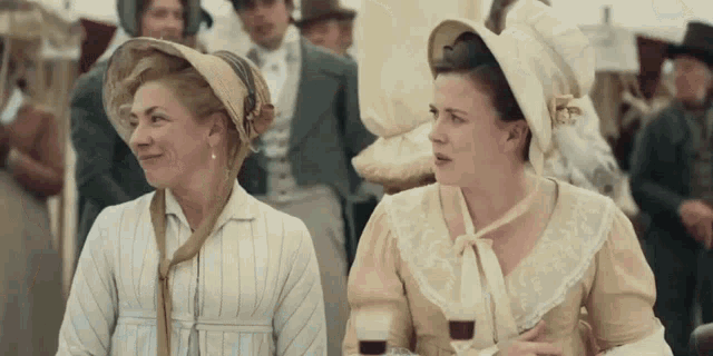 two women are sitting next to each other in a crowd and one is holding a glass of wine