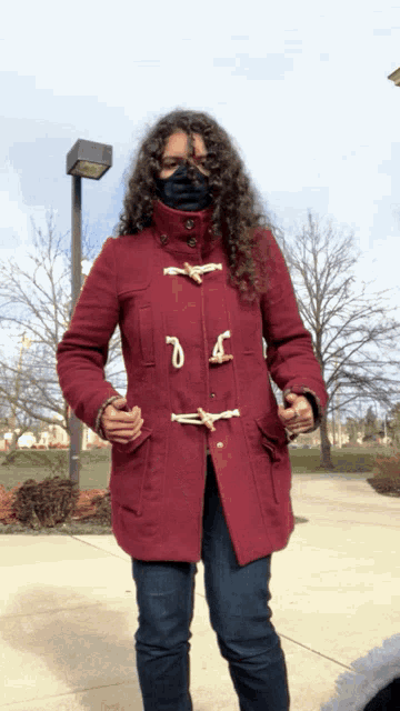 a woman wearing a mask and a red coat with toggles