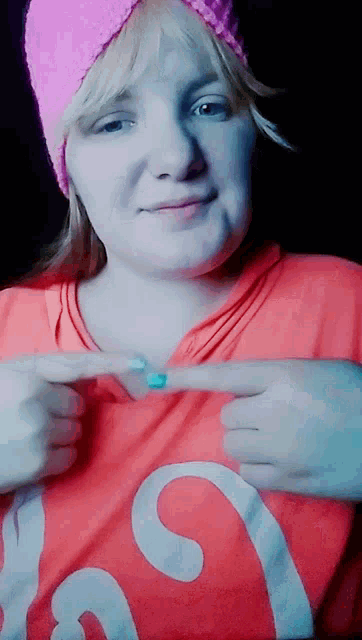 a woman wearing a pink hat and a red shirt is pointing at her breast