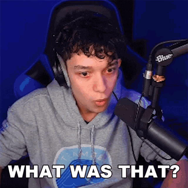 a man wearing headphones is sitting in front of a microphone and saying what was that .