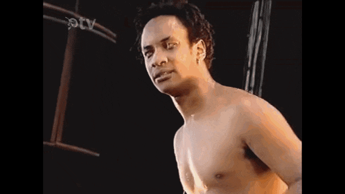 a man without a shirt is standing in front of a black background and looking at the camera .