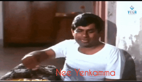 a man in a white shirt is sitting at a table with the words nee yenkamma written in red