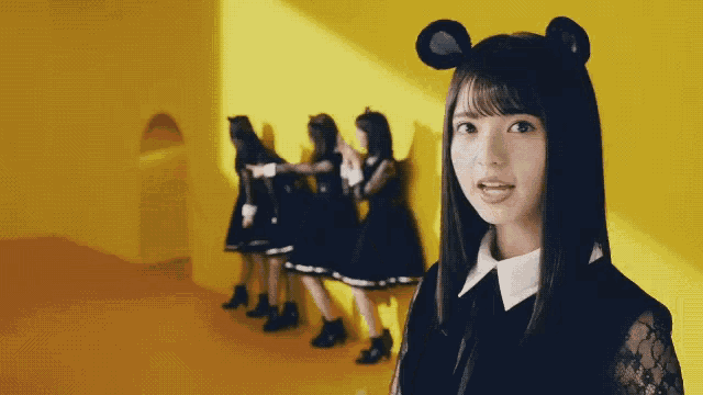 a woman wearing a mouse ear headband is standing in front of a yellow wall