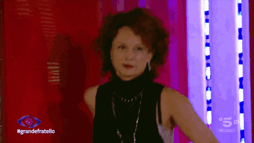 a woman in a black top is standing in front of a red wall with the words grandefratello on the bottom