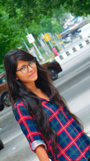 a woman wearing glasses and a plaid shirt stands in front of a street