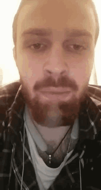 a man with a beard wearing headphones and a plaid shirt is making a funny face .