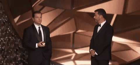 two men in suits and ties are standing next to each other on a stage in front of a christmas tree .