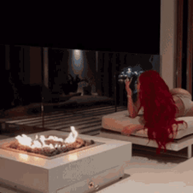 a woman with red hair is laying on a bed next to a fire pit