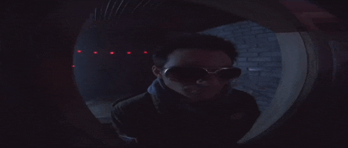 a man wearing sunglasses is looking through a hole in a wall