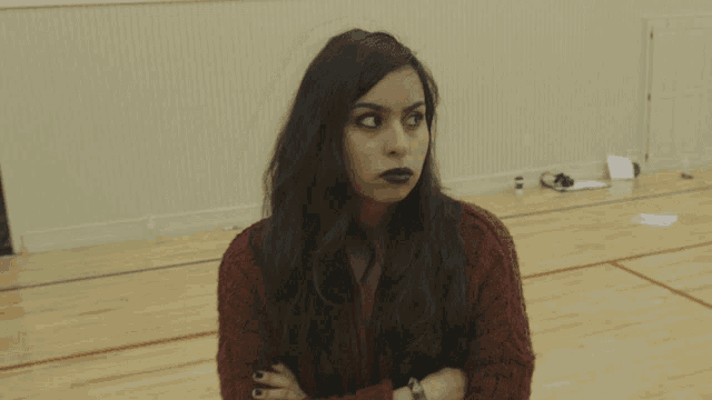 a woman in a red sweater has her arms crossed and has black lipstick on her lips