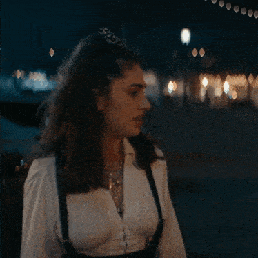 a woman wearing suspenders and a white shirt is walking down a street at night