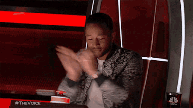 a man is clapping his hands in front of a sign that says #thevoice