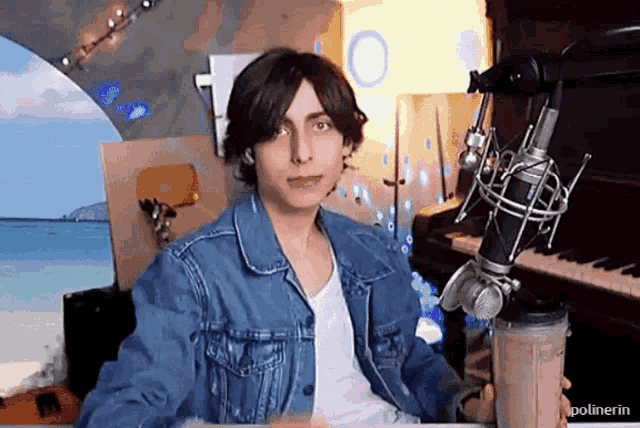 a man in a denim jacket is holding a milkshake in front of a piano