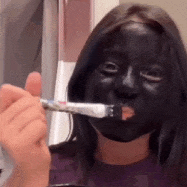 a woman with a black mask on her face is brushing her teeth with a toothpaste .