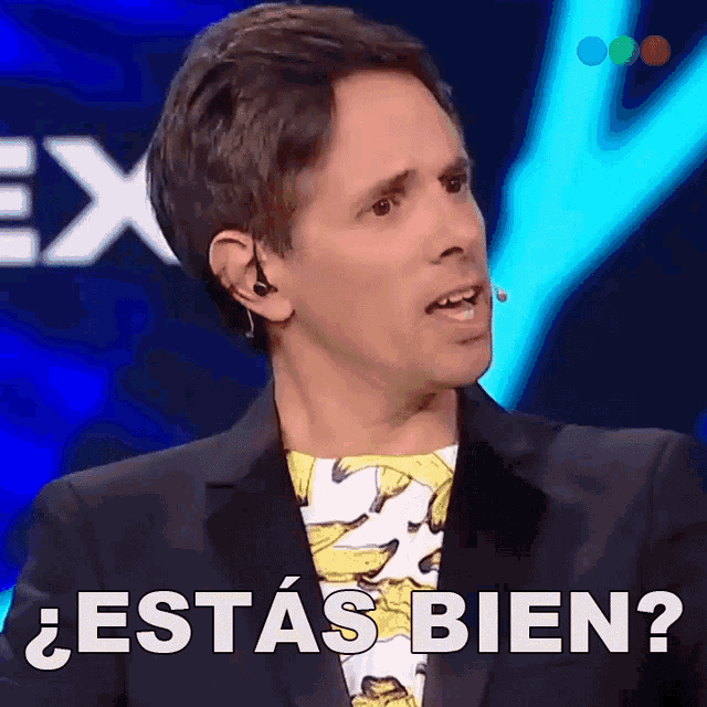 a man wearing a banana shirt says " estas bien " in front of a microphone