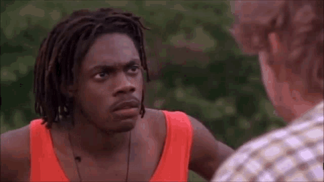 a man with dreadlocks is standing next to another man in a red tank top .