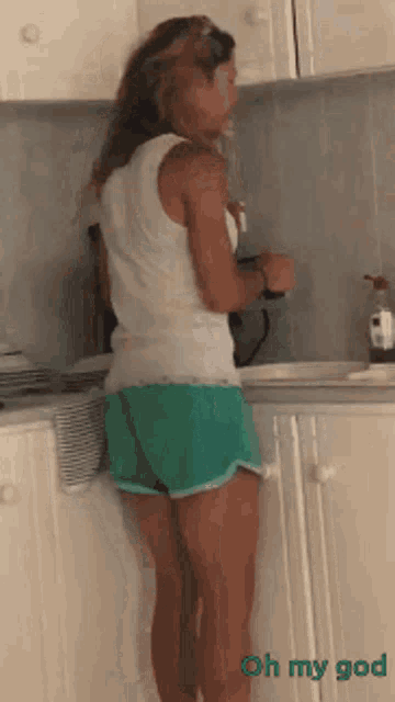 a woman in shorts and a tank top is standing in a kitchen