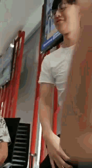 a man wearing glasses and a white t-shirt is standing in front of a television .