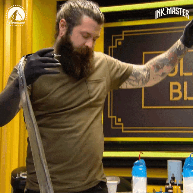 a man with a beard and tattoos is standing in front of a sign that says ink master