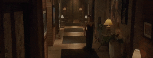 a man and a woman are walking in a dark room . the woman is wearing a black dress and earrings .