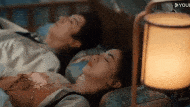 a man and a woman are sleeping next to each other in a bed next to a lamp .